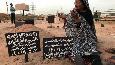 Getty Images Khadom, the mother of Al-Moez visits the tomb of her son, killed when a bullet pierced the window of his workplace and lodged itself in his heart during an anti-government demonstration in the Sudanese capital Khartoum in April, on July 9, 2019. - Like dozens of others who lost a son, uncle or brother, Al-Moez' family has paid a high price for Sudan's revolution that toppled its longtime autocratic ruler Omar al-Bashir in April.