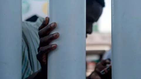 Getty Images A man part group of asylum seekers, mostly from African countries, checks his phone as he waits for a negotiation commission to walk out El Chaparral port of entry during a protest in Tijuana, Baja California state on July 9, 2019, northwestern Mexico. - Asylum seekers claimed that Mexican migration officers were selling spots on the line to get an interview with US migration authorities.