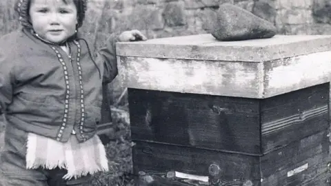 Hoods Honey Stuart Hood as a toddler next to a bee hive