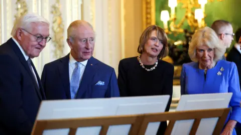 Reuters The King and Queen stand in an ornate room beside the German president and his wife. They are stood in a row in front of a wooden stand on which several white sheets stand. 