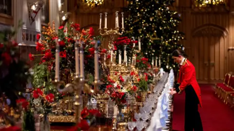 PA Media A staff member in a red coat sets up a long, ornately decorated table for the banquet